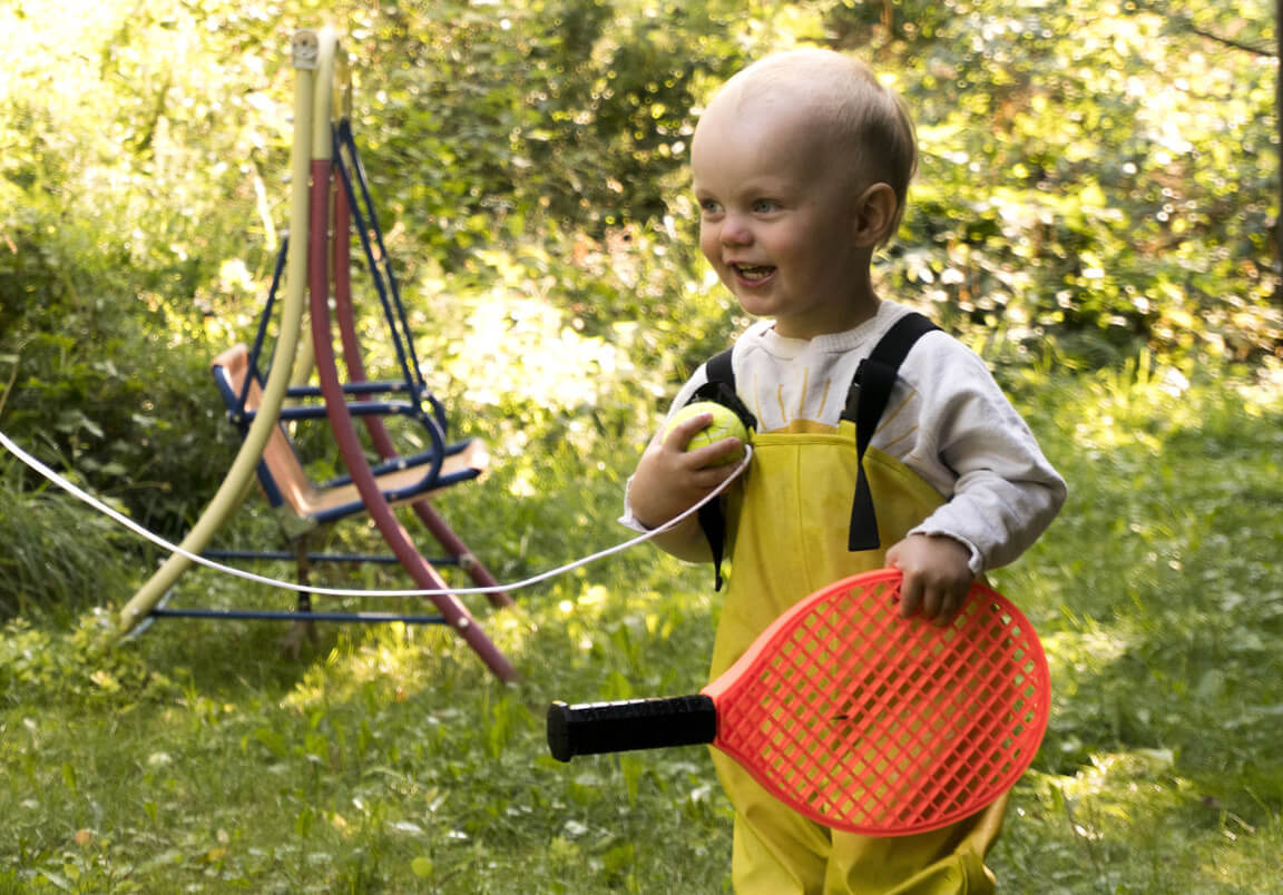 Barnet leker ute med en racket i handen.