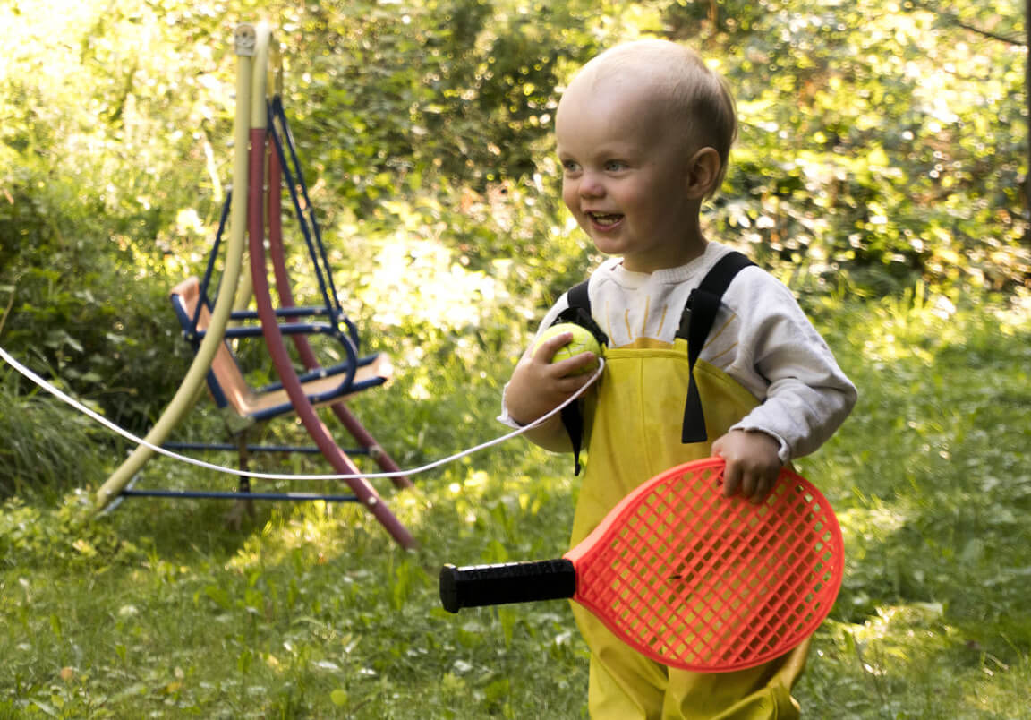 Lapsi leikkii ulkona nurmikolla pelimaila kädessään.