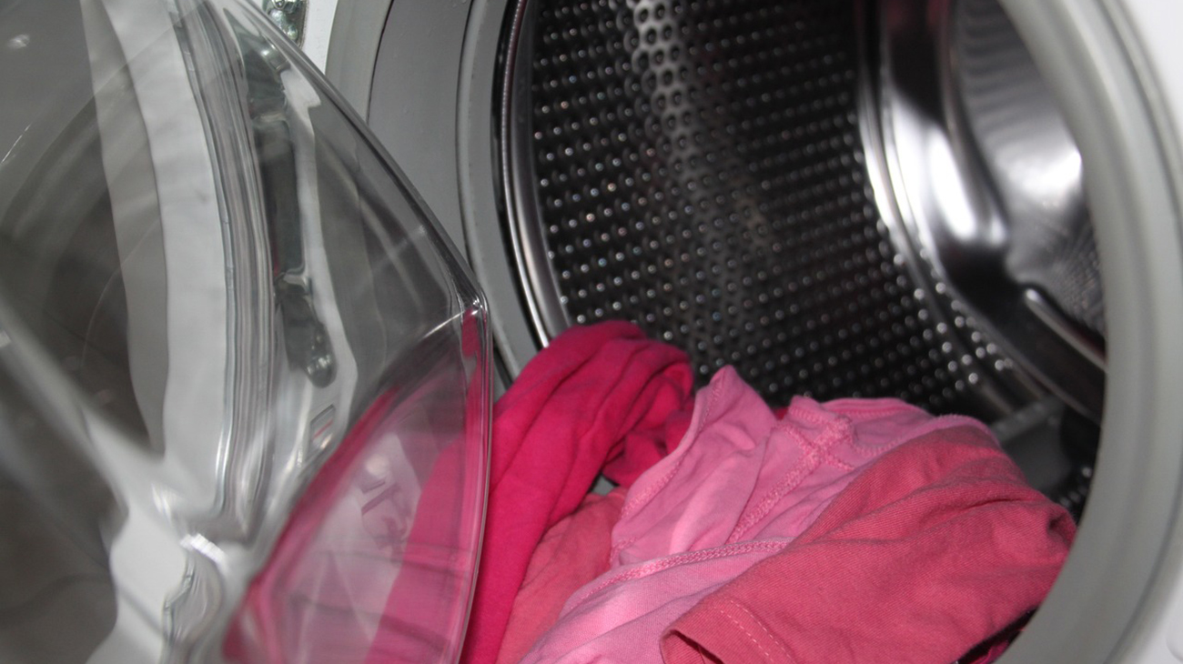 Avonainen pyykinpesukone, luukusta pursuaa pinkkejä vaatteita.