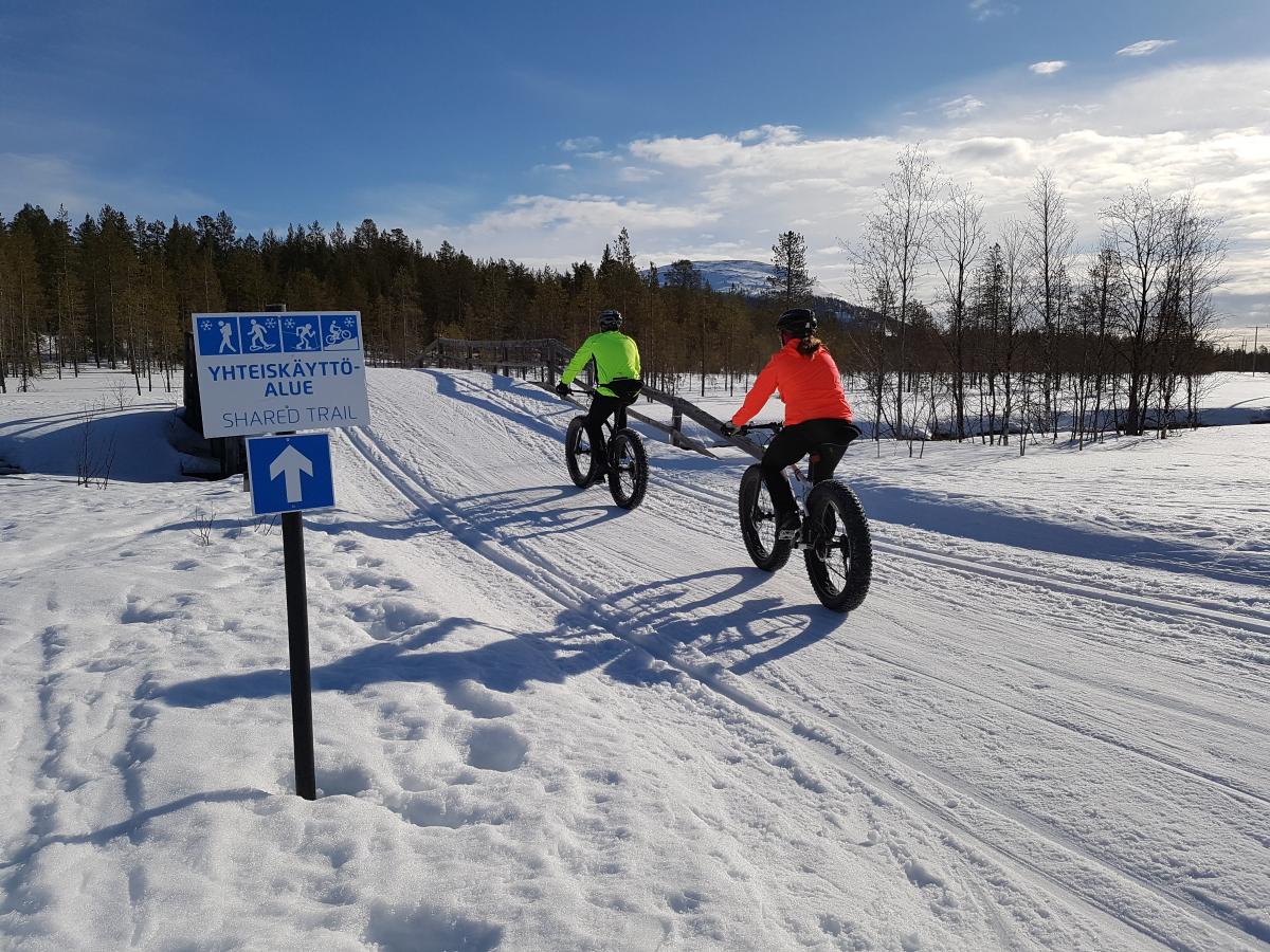 Kaksi pyöräilijää Fatbike-pyörillä ajaa lumisella monitoimireitillä.