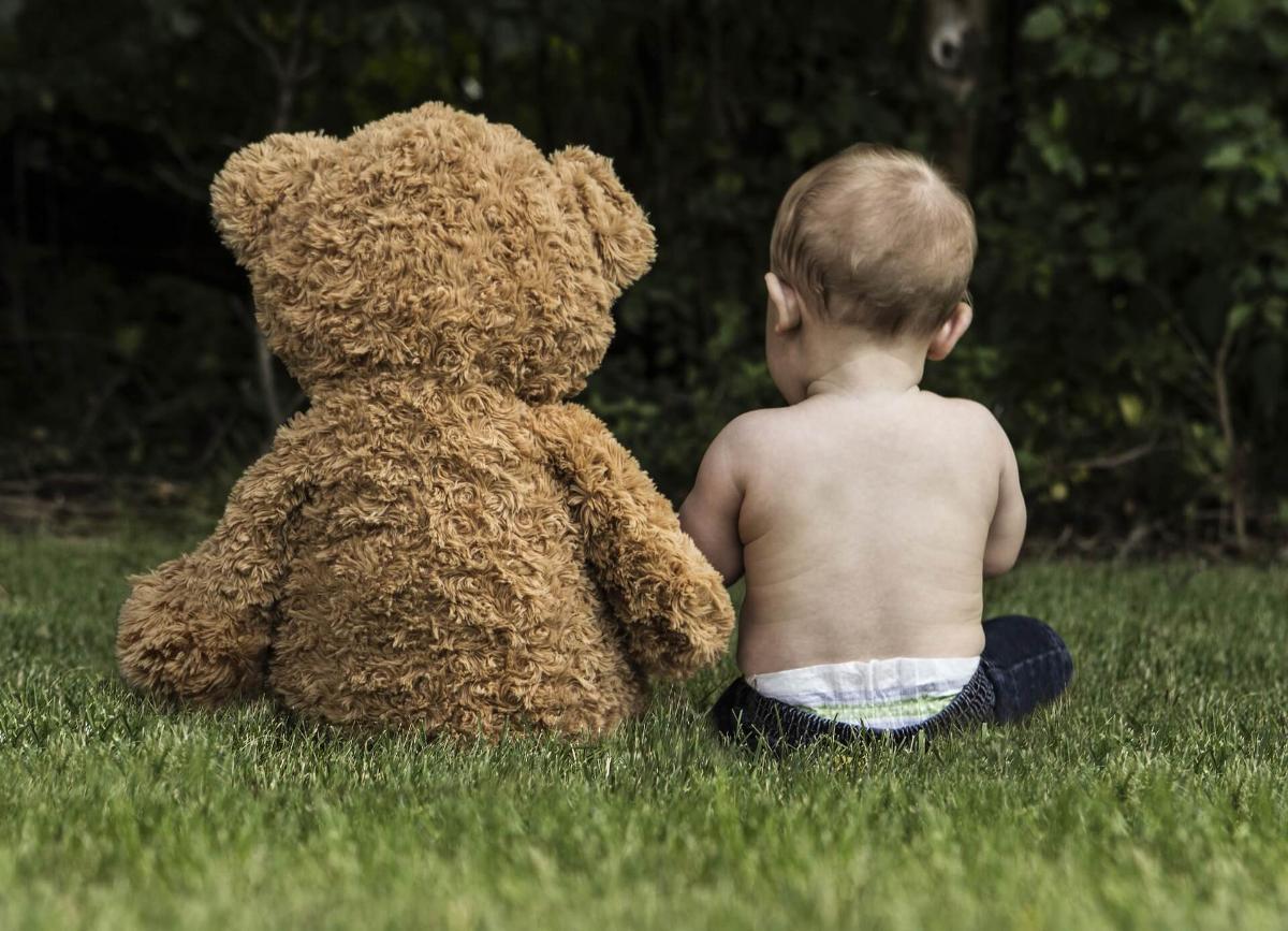Lapsi istuu nurmikolla teddykarhun kanssa.