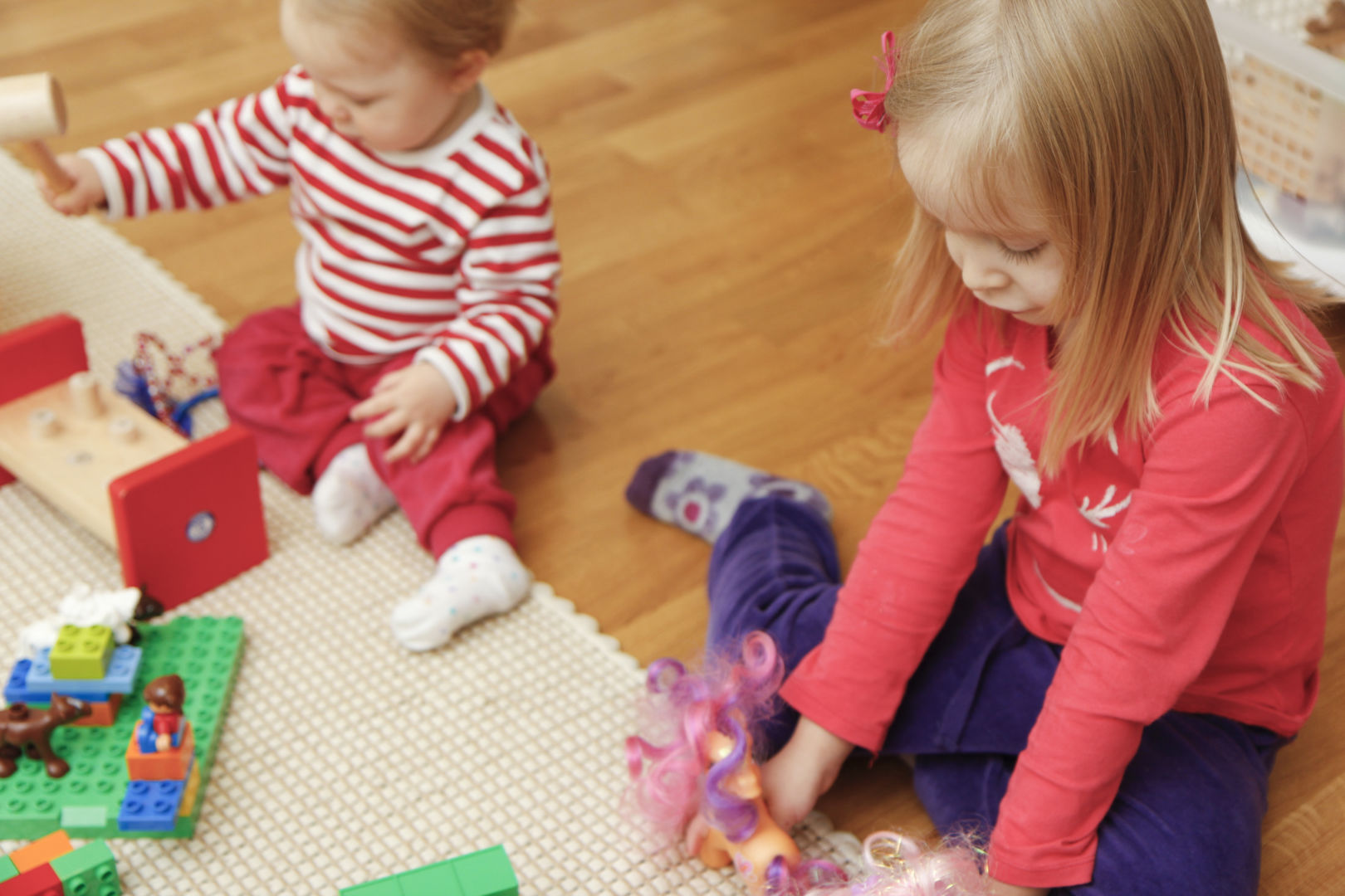 Lapset leikkivät lattialla erilaisilla leluilla.